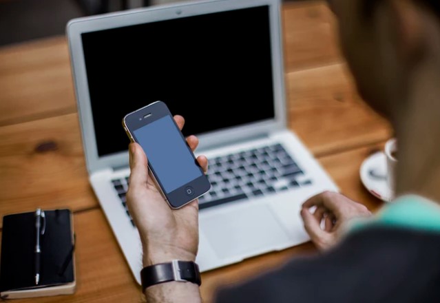 Computer telecommunication Man holds iPhone in his hand in front of laptop
