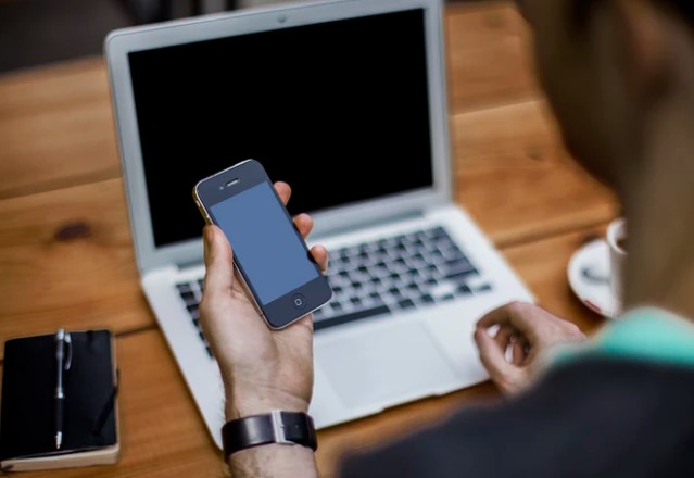 Man holds iPhone in his hand in front of laptop